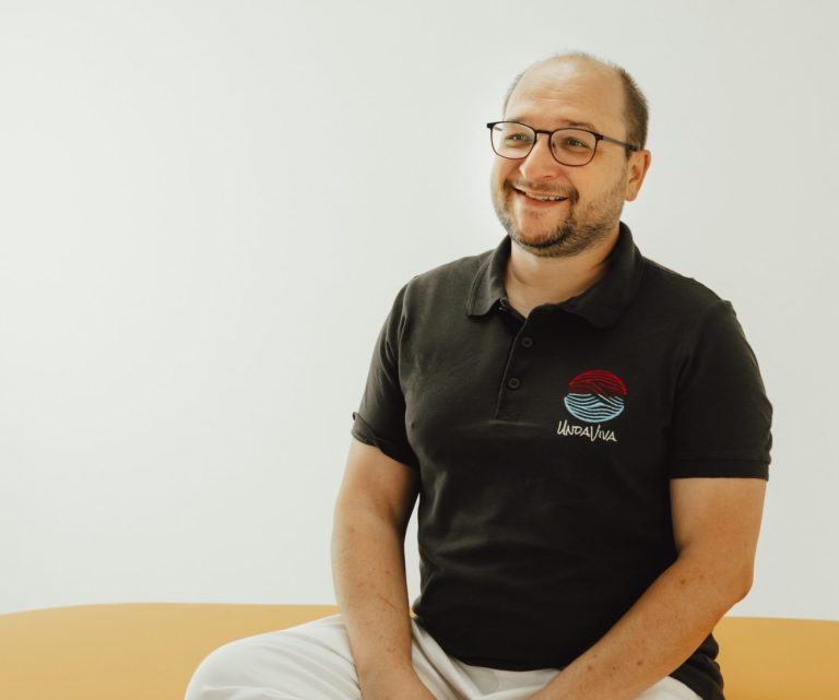 Markus Hayer von UndaViva sitzt freundlich auf einer Massageliege.
